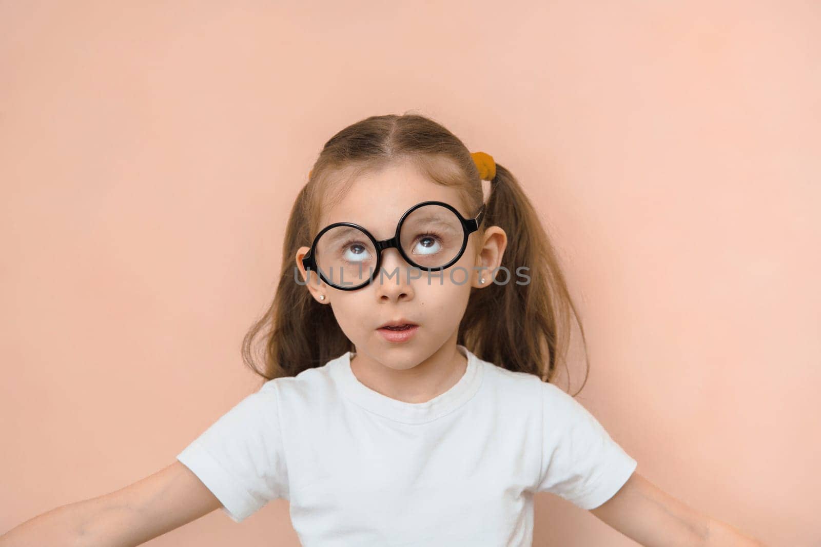 Confused funny little girl of primary school age with crooked round glasses.