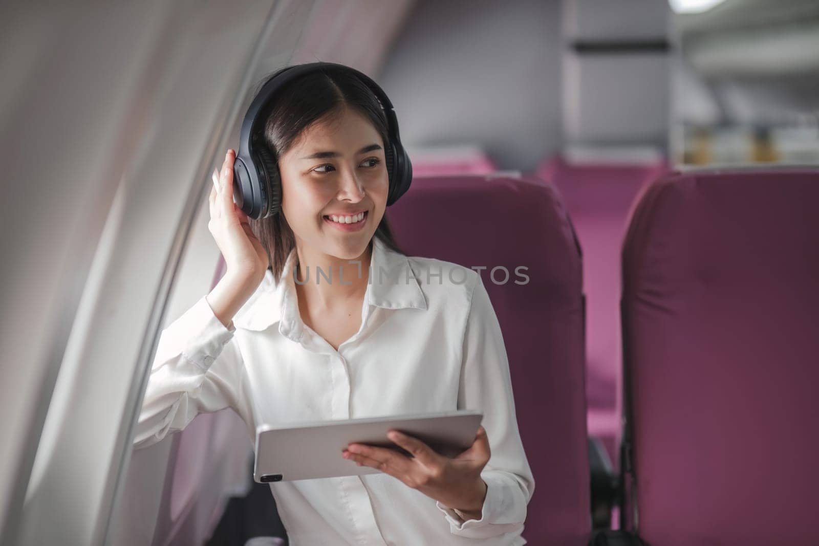 Asian young woman using tablet sitting near windows at first class on airplane during flight,Traveling and Business concept by wichayada