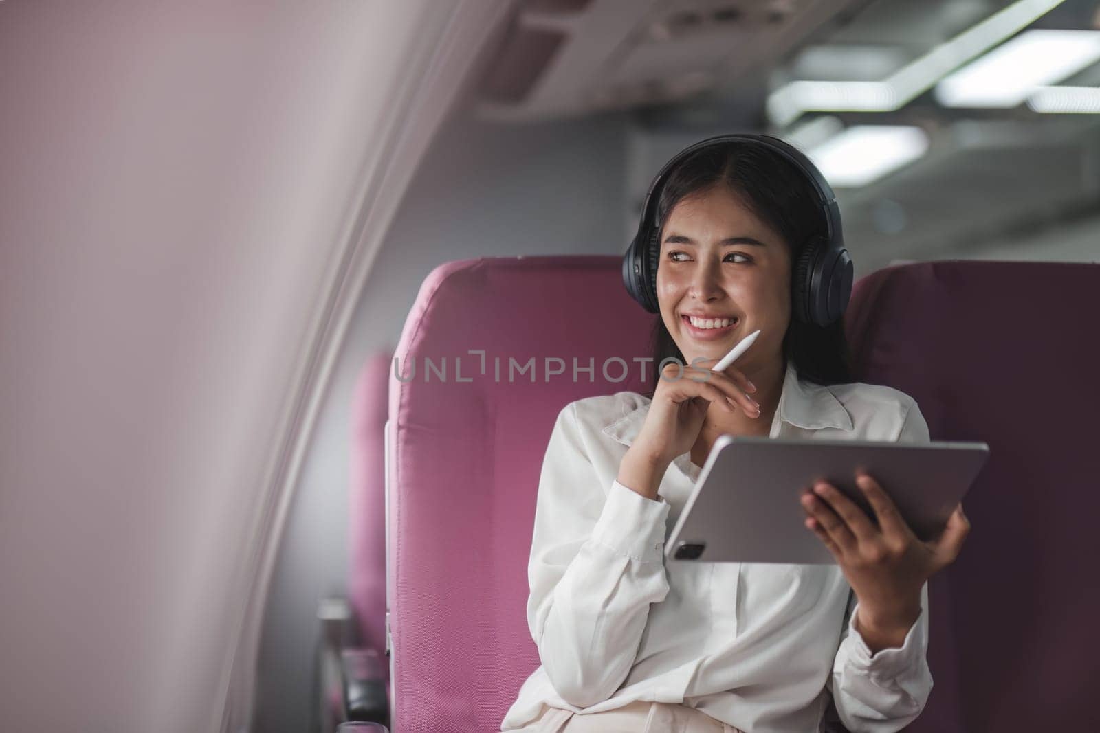 Asian young woman using tablet sitting near windows at first class on airplane during flight,Traveling and Business concept..