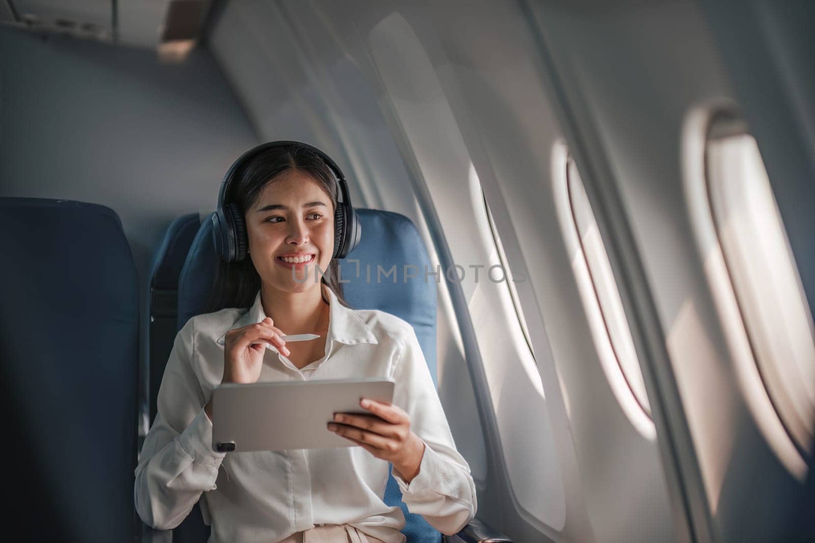 Asian young woman using tablet sitting near windows at first class on airplane during flight,Traveling and Business concept..