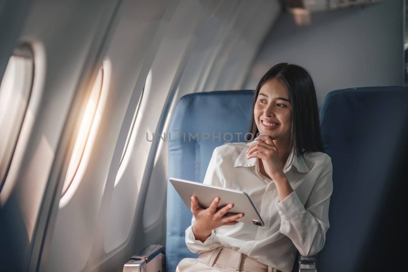 Asian young woman using tablet sitting near windows at first class on airplane during flight,Traveling and Business concept by wichayada