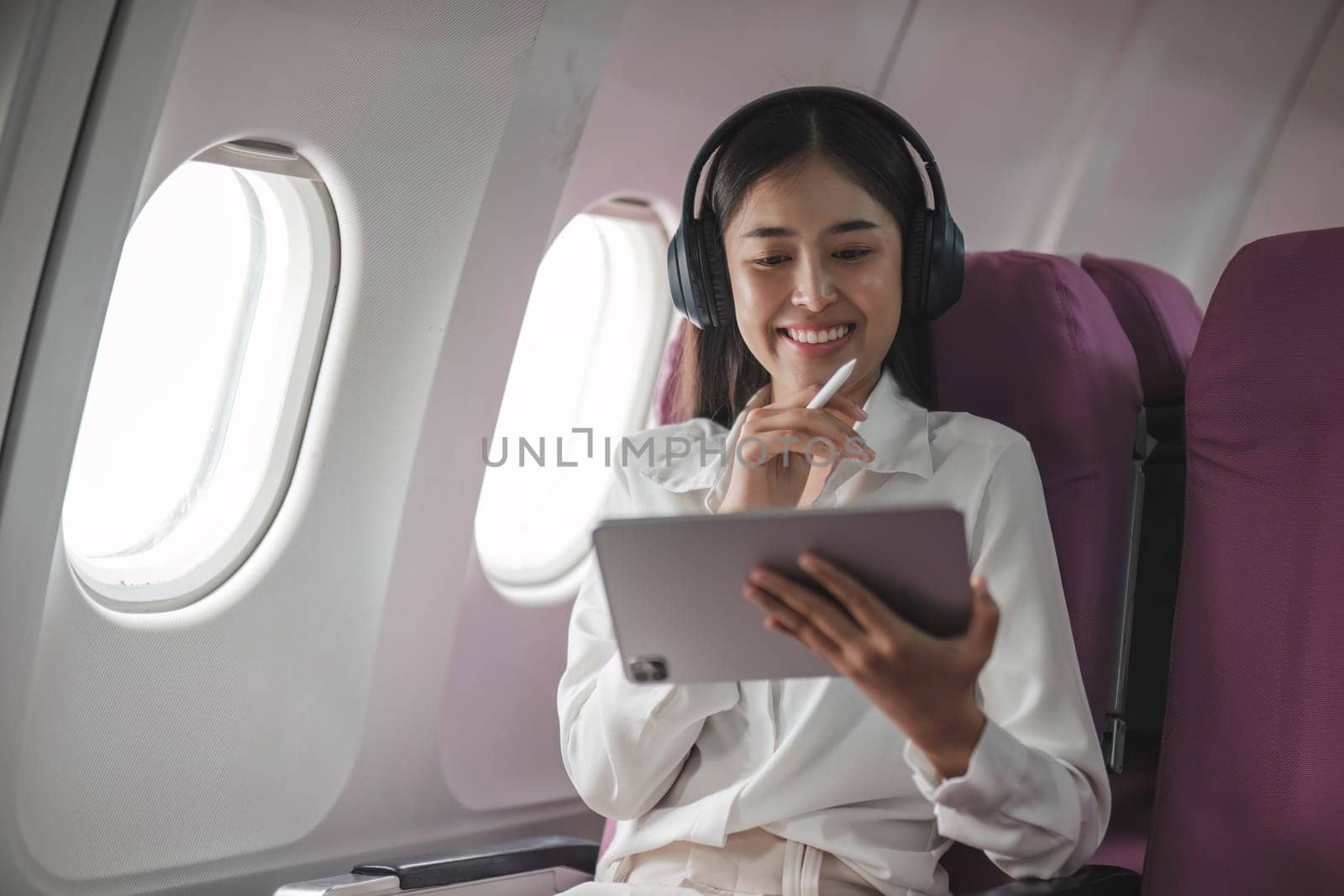 Asian young woman using tablet sitting near windows at first class on airplane during flight,Traveling and Business concept by wichayada