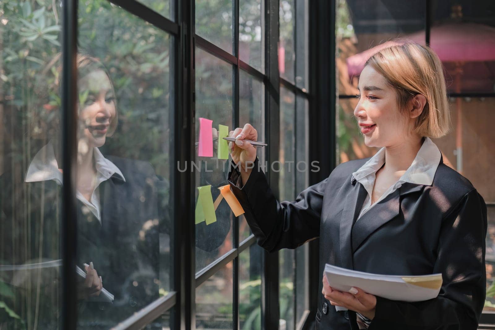 Young businesswoman creative team using post it notes in glass wall to writing strategy business plan to development grow to success...