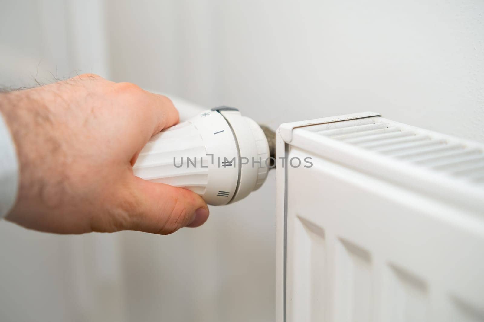 Man hand regulates temperature knob of the heating radiator to reduce heating costs.