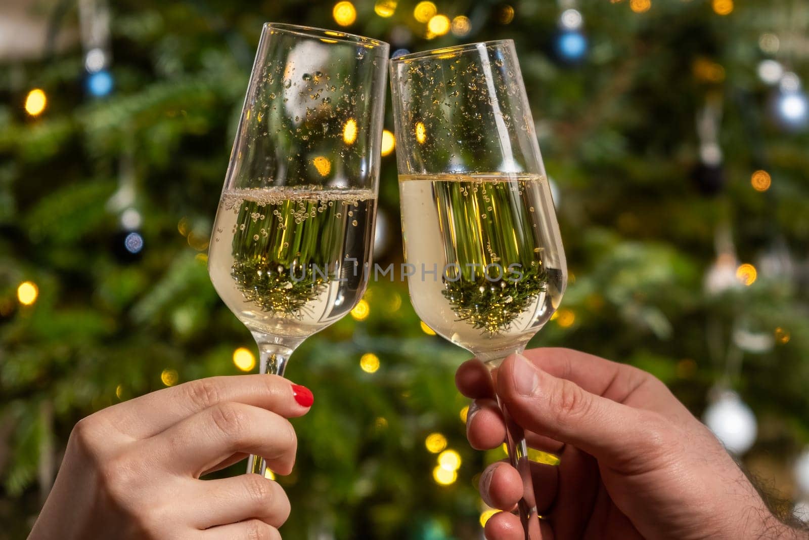Man and woman clinking glasses with champagne against the Christmas tree. Celebrating the atmosphere of the New Year party.