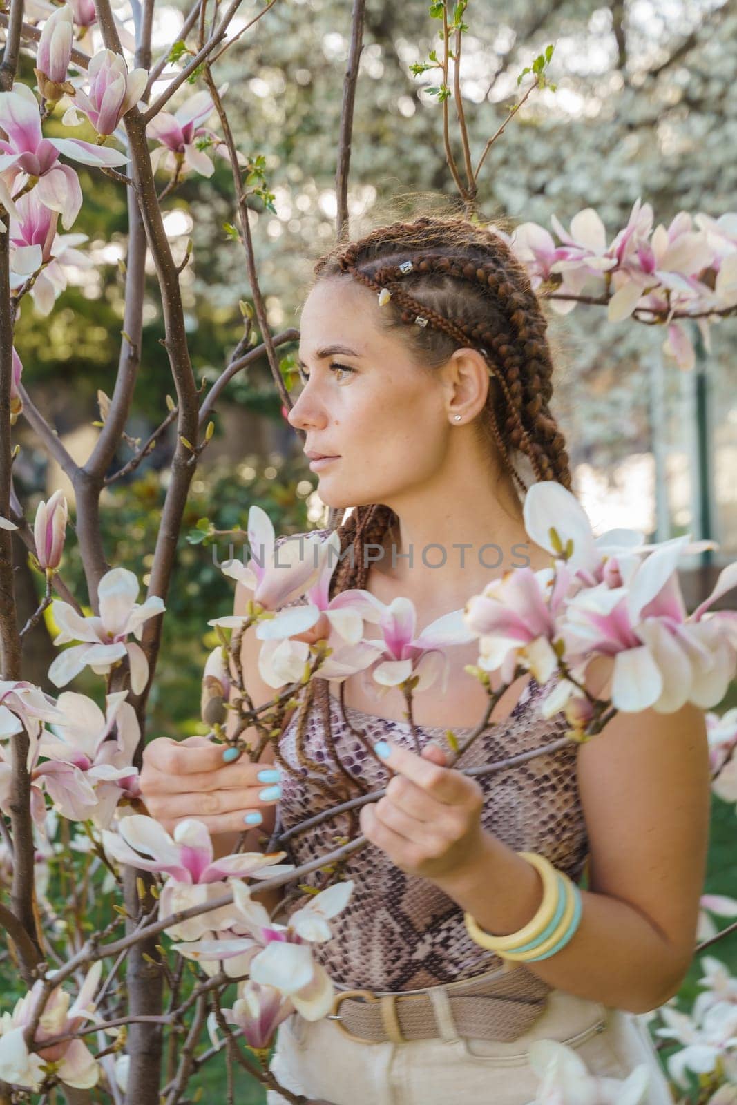 Magnolia flowers. Happy woman enjoys by blooming magnolia tree and sniffs it flowers with closed eyes in spring garden. Portrait