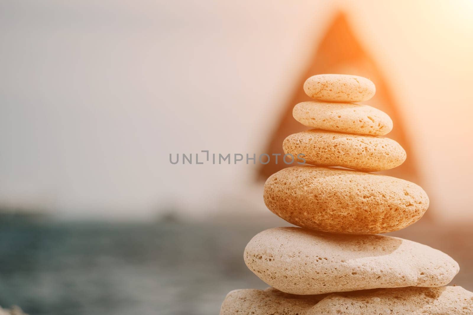 Pyramid stones on the seashore with warm sunset on the sea background. Happy holidays. Pebble beach, calm sea, travel destination. Concept of happy vacation on the sea, meditation, spa, calmness.