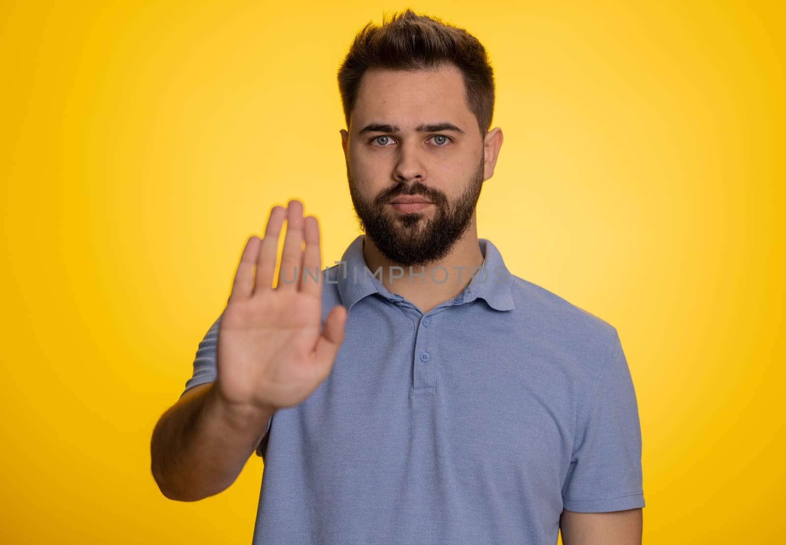 Angry man say No hold palm folded crossed hands in stop gesture, warning of finish, prohibited access, declining communication, body language, danger. Young guy on yellow background. People lifestyle