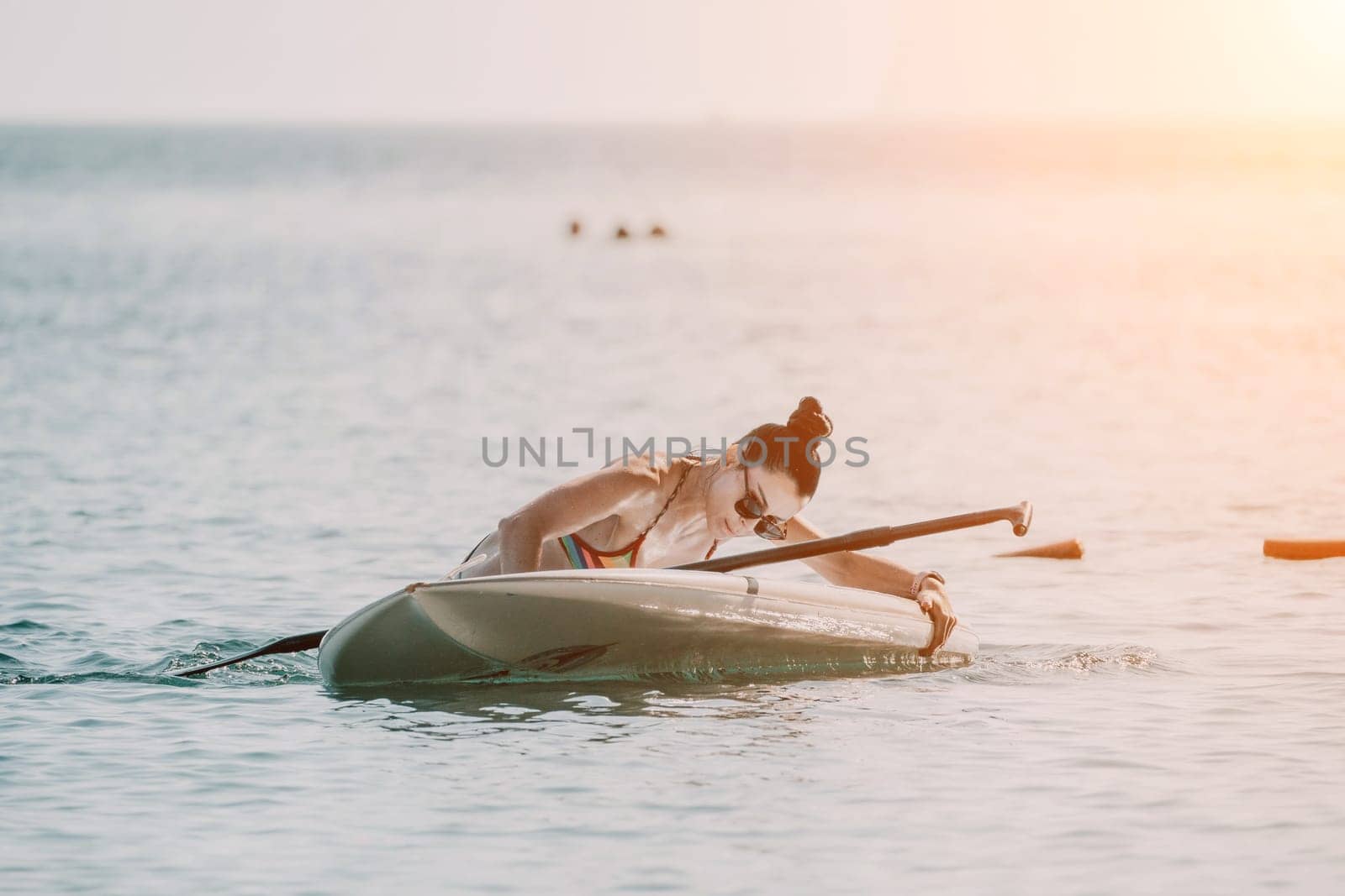 Sea woman sup. Silhouette of happy middle aged tanned woman in rainbow bikini, surfing on SUP board, confident paddling through water surface. Idyllic sunset. Active lifestyle at sea or river. by panophotograph
