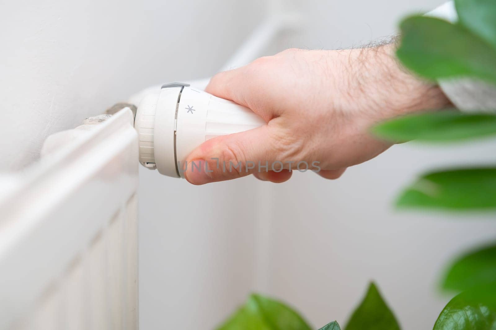 Man hand regulates temperature knob of the heating radiator to reduce heating costs.