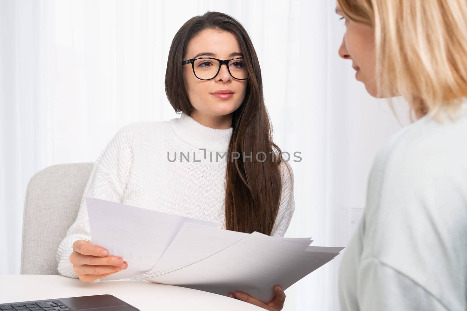 Young and beautiful insurance agent in glasses consulting client and shows documents