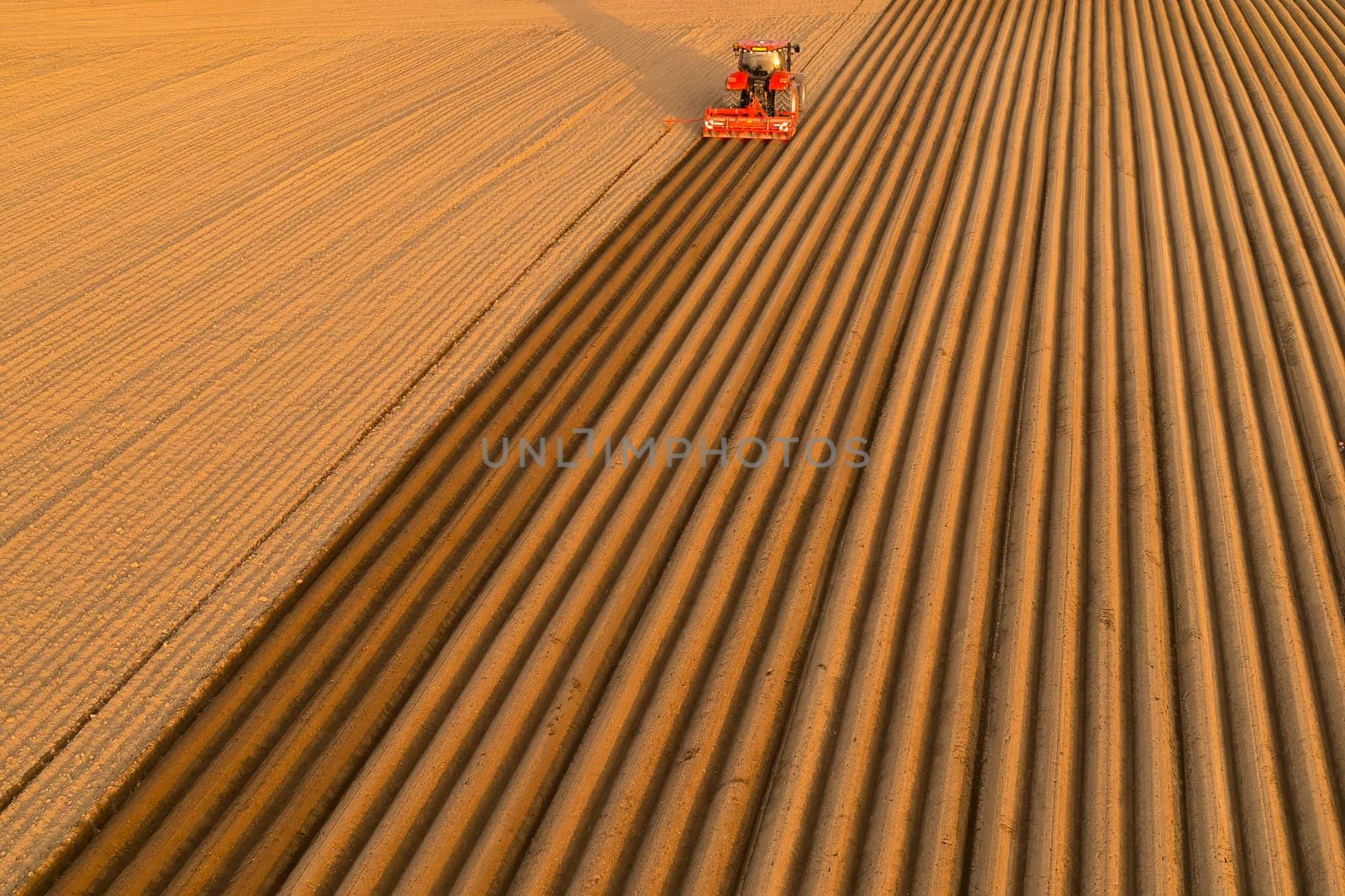 Aerial view of tractor making furrows on soil at agricultural field at sunset, April 2022, Prague, Czech Republic