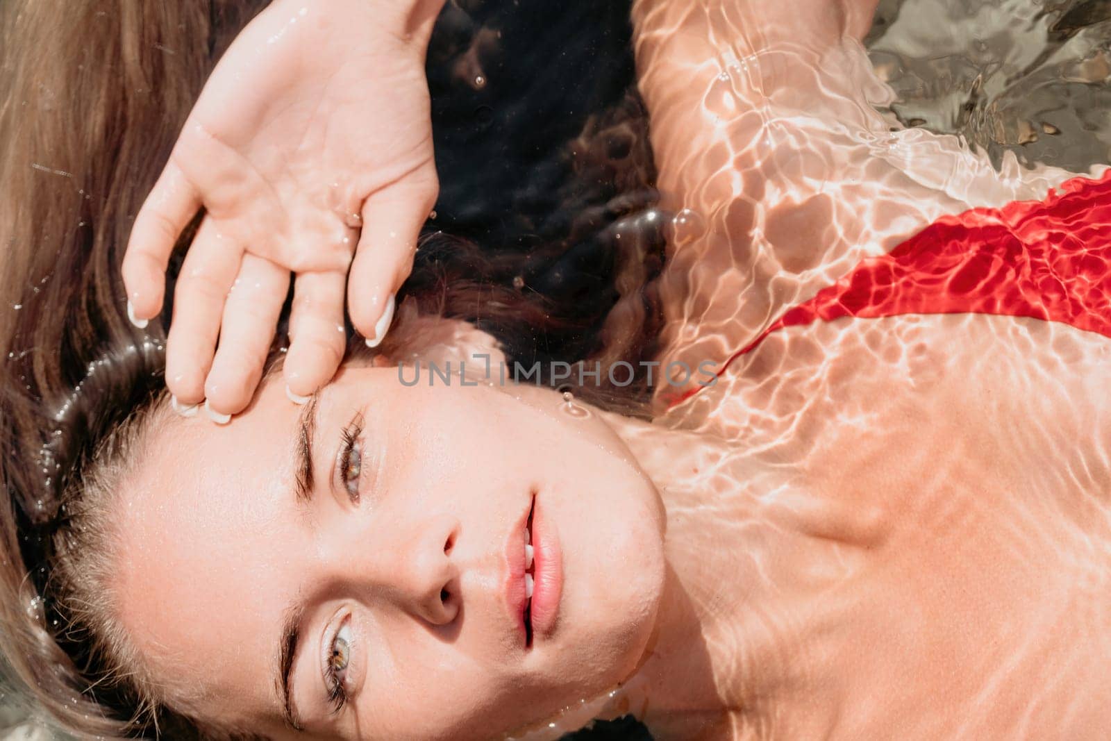 Woman travel portrait. close-up portrait of a happy woman with long hair in a red bikini, floating in water and smiling at the camera. by panophotograph