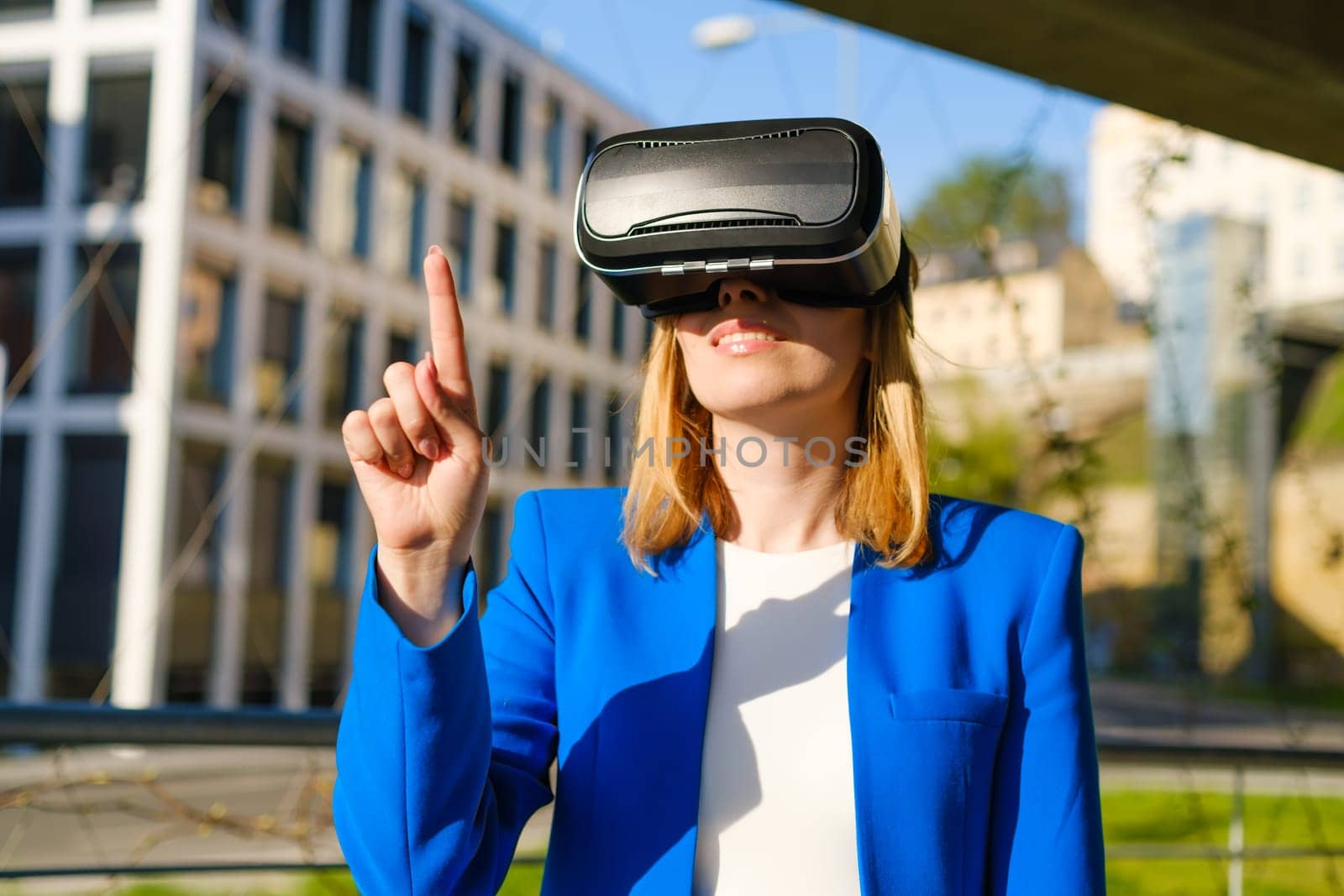 Young woman touching the air using a virtual interface by pressing buttons finger in virtual reality glasses near business center.