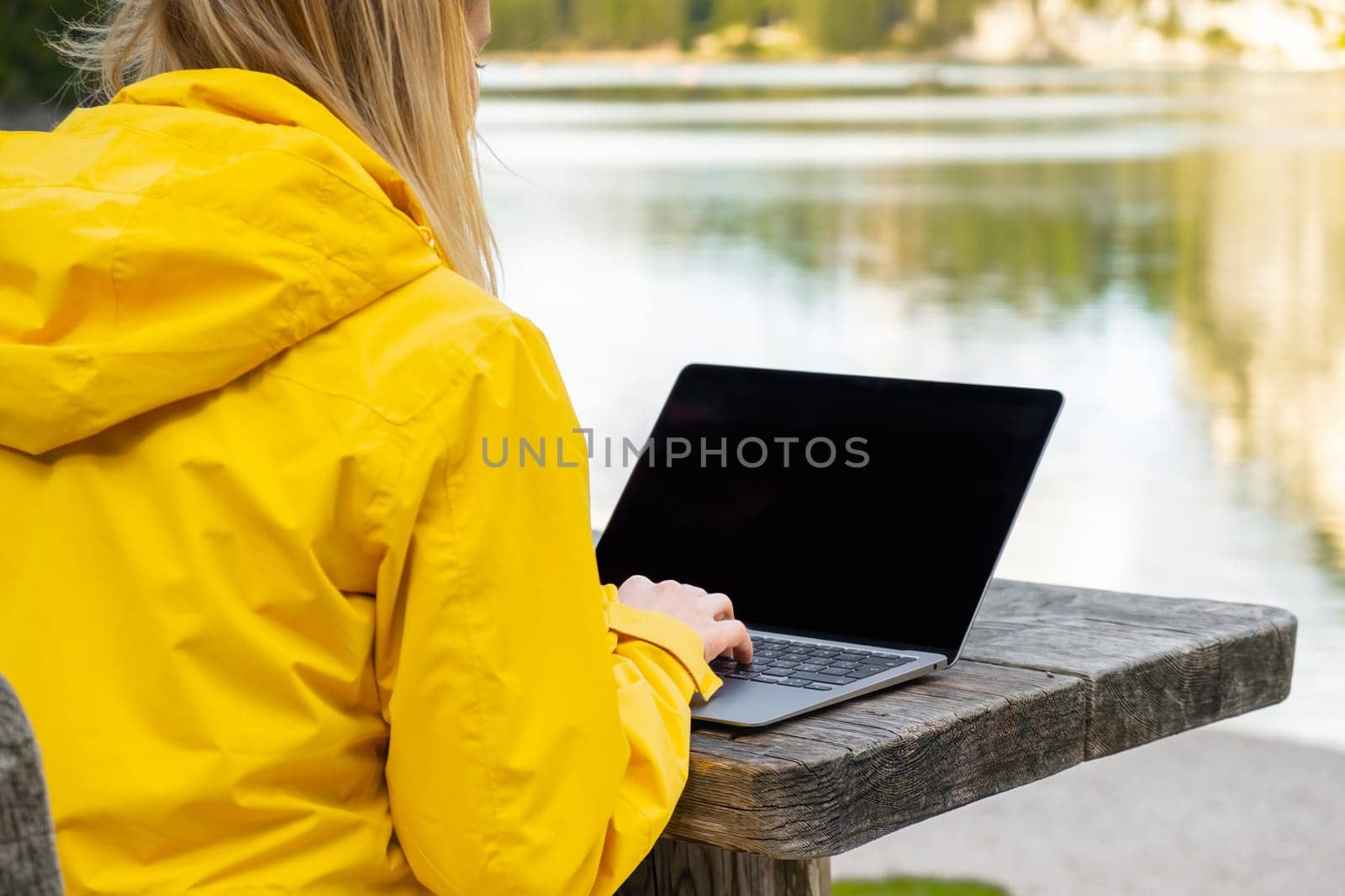 Remote worker relaxing near the lake and using a laptop. Working or studying over a laptop and smartphone.