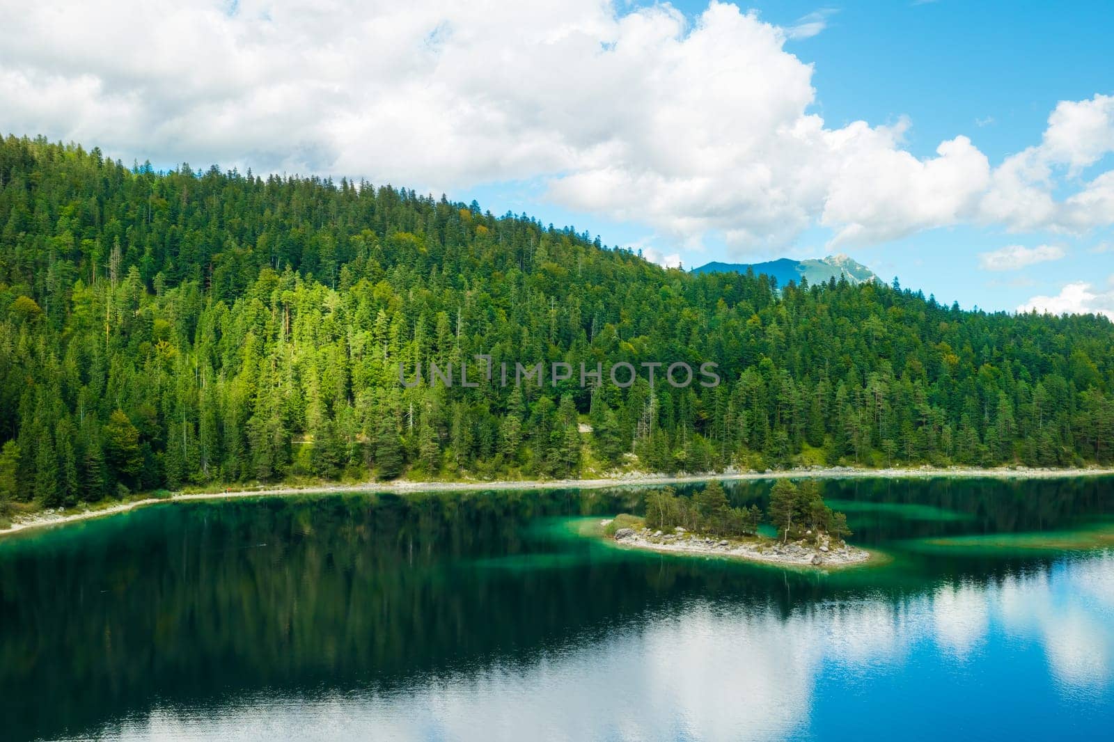Mountains with spruce trees and clouds are reflected in a forest river. Summer landscape of a riverside.