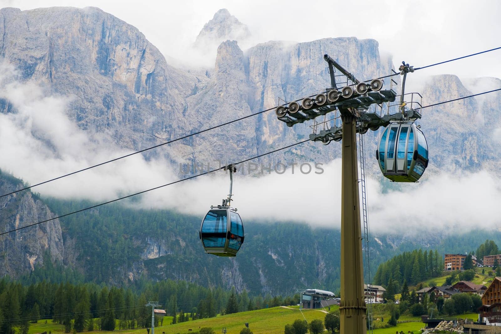 Two cable way cabins against the Dolomites covered with clouds.
