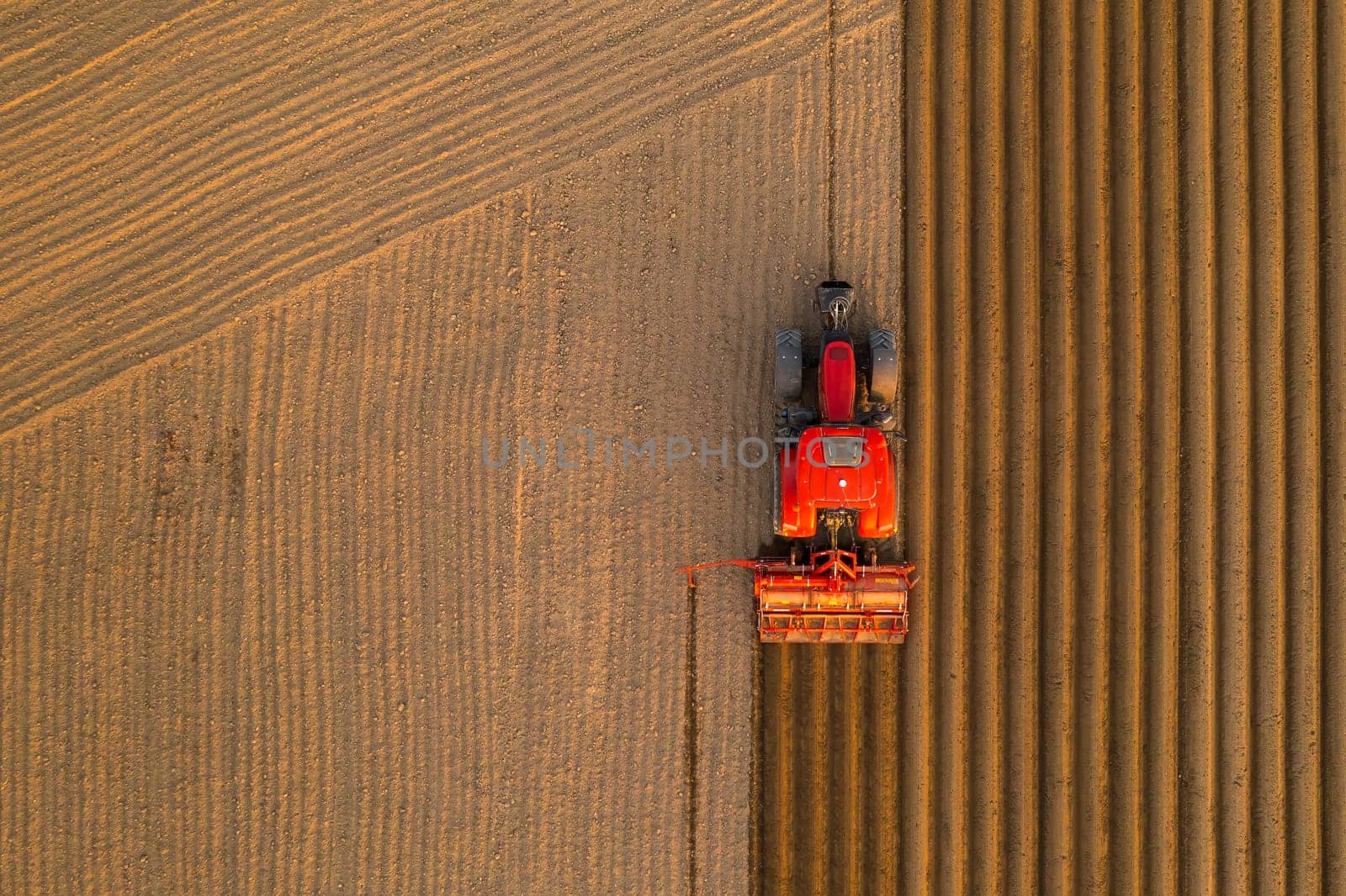 PRAGUE , CZECH REPUBLIC - MARCH 18 2022: Tractor drives preparing beds for planting seedlings in cultivated soil. Heavy machine tills on field helping with agriculture aerial view