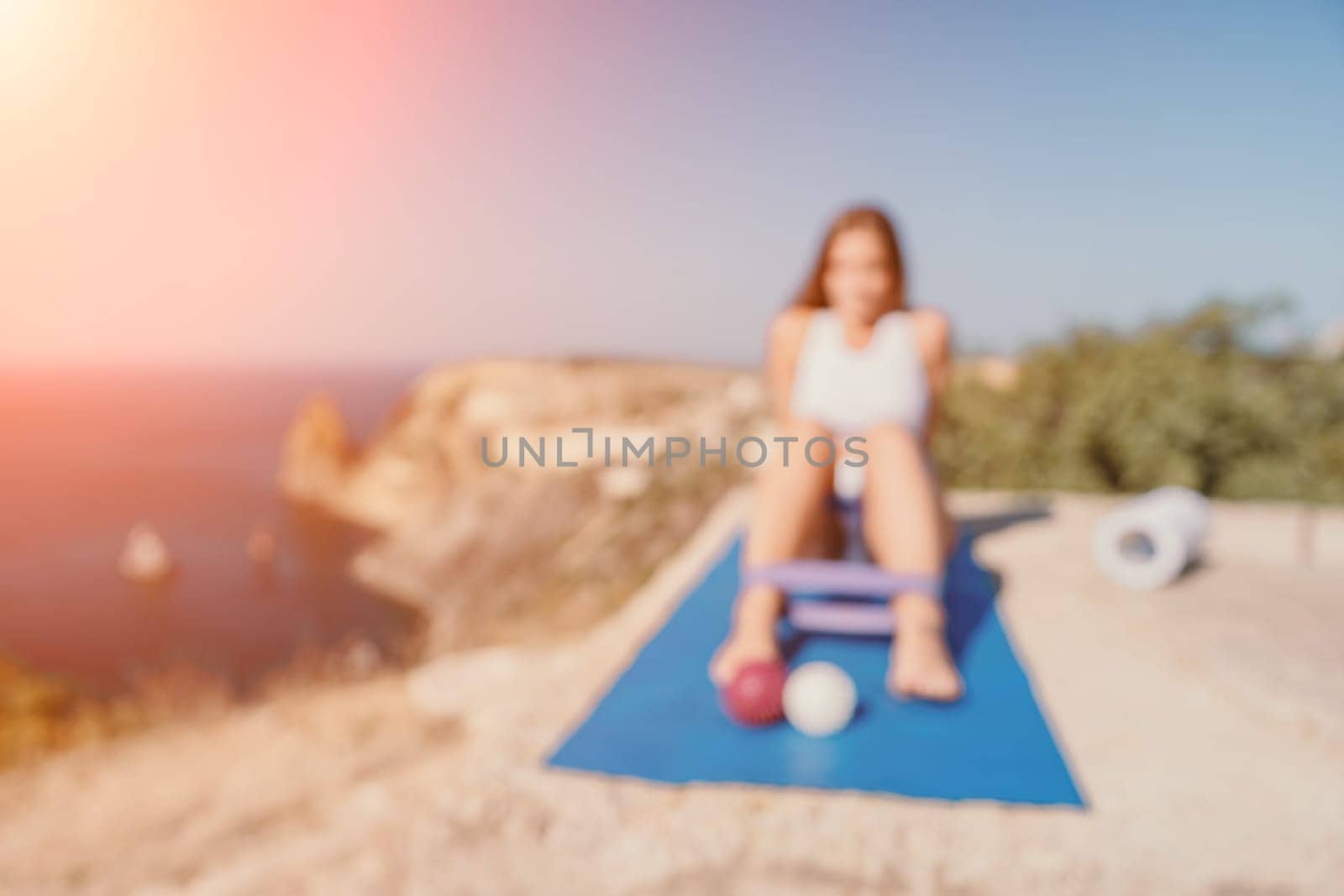 Abstract defocused Woman sea pilates. Sporty happy woman practicing fitness on yoga mat with rubber band, massage balls and roller near sea, active female outside, enjoying healthy lifestyle by panophotograph