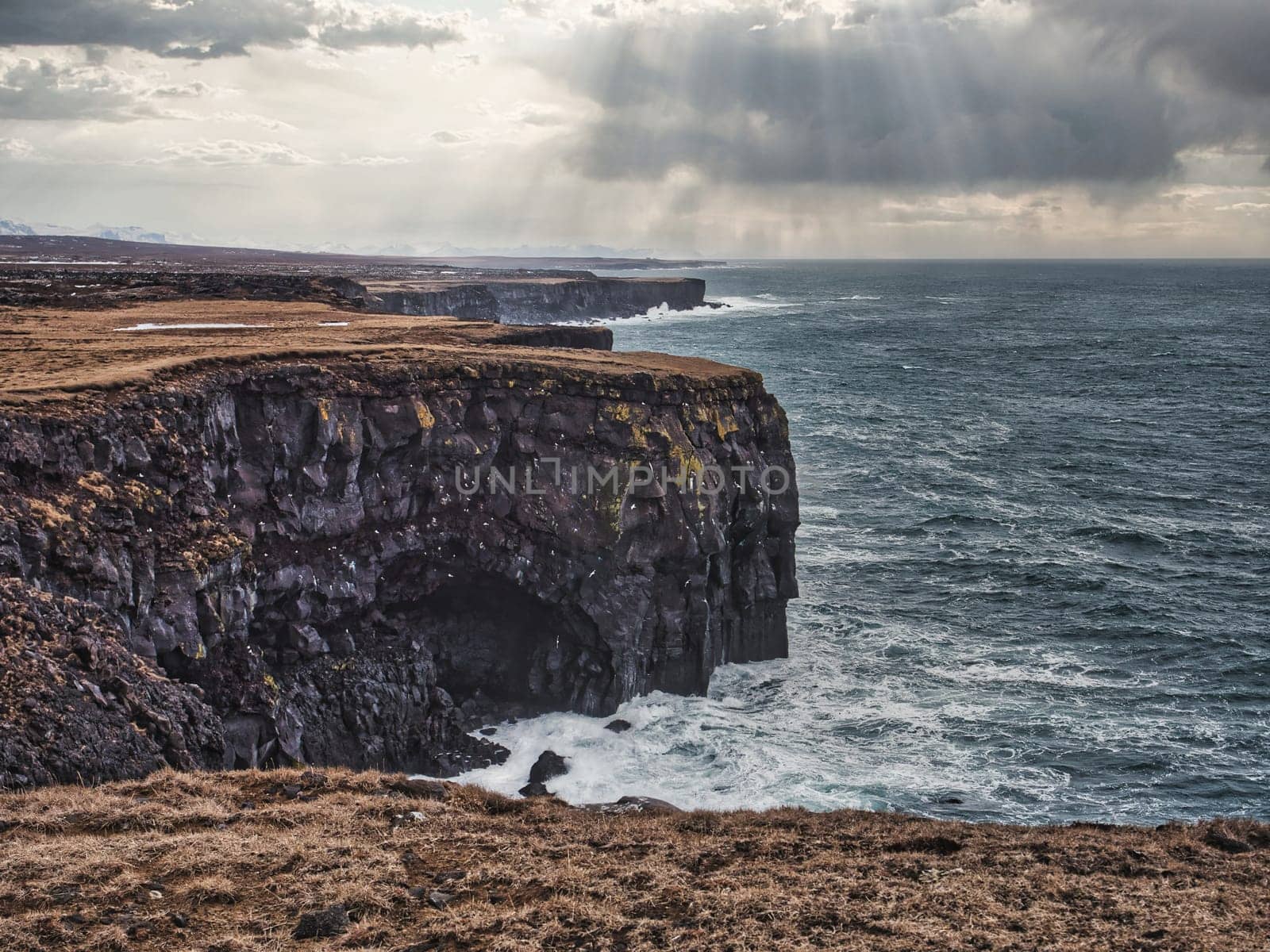 Cold sea water crashing against rocks near rough stony cliffs, on stormy day in Iceland