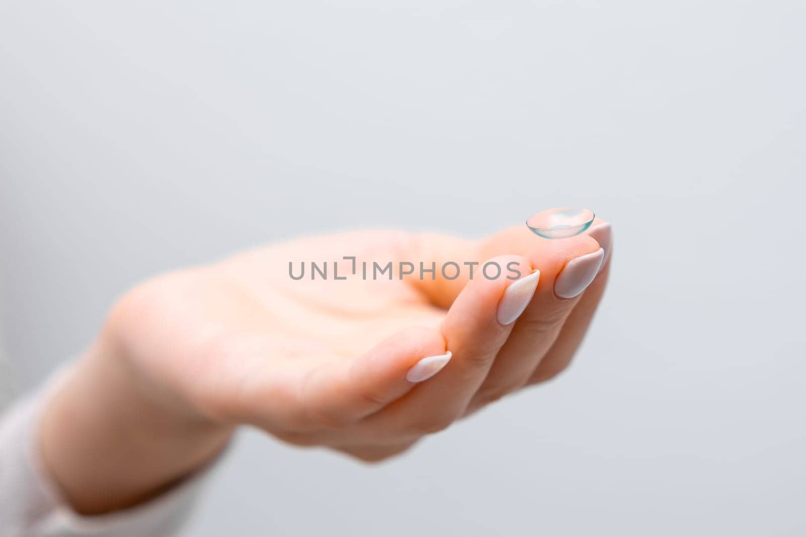 Close up woman hand with contact lens on the grey background