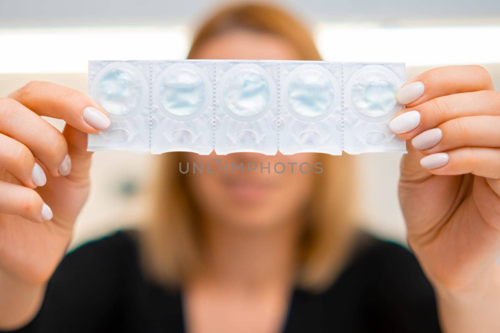 Smiling woman holding a blister with eye lenses in front of yourself. Disposable eye lenses in the solution.