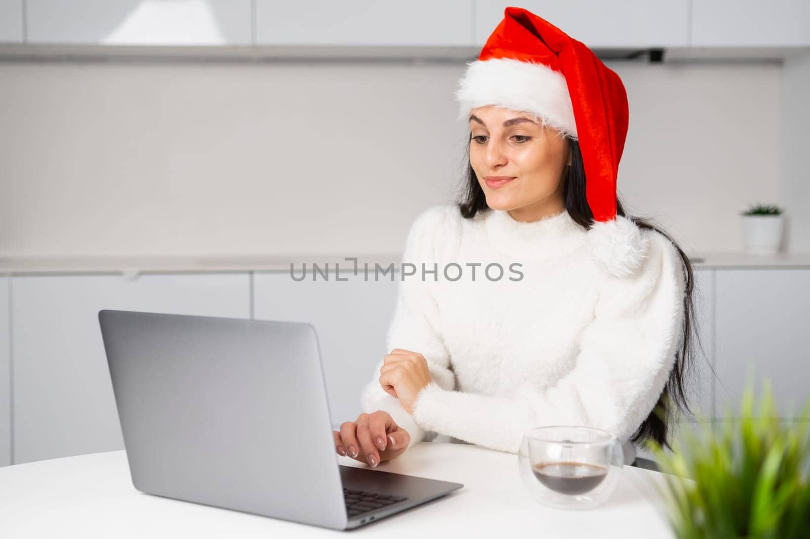 Cute Santa Claus woman working at home using a notebook. Freelancer works on Christmas holidays.