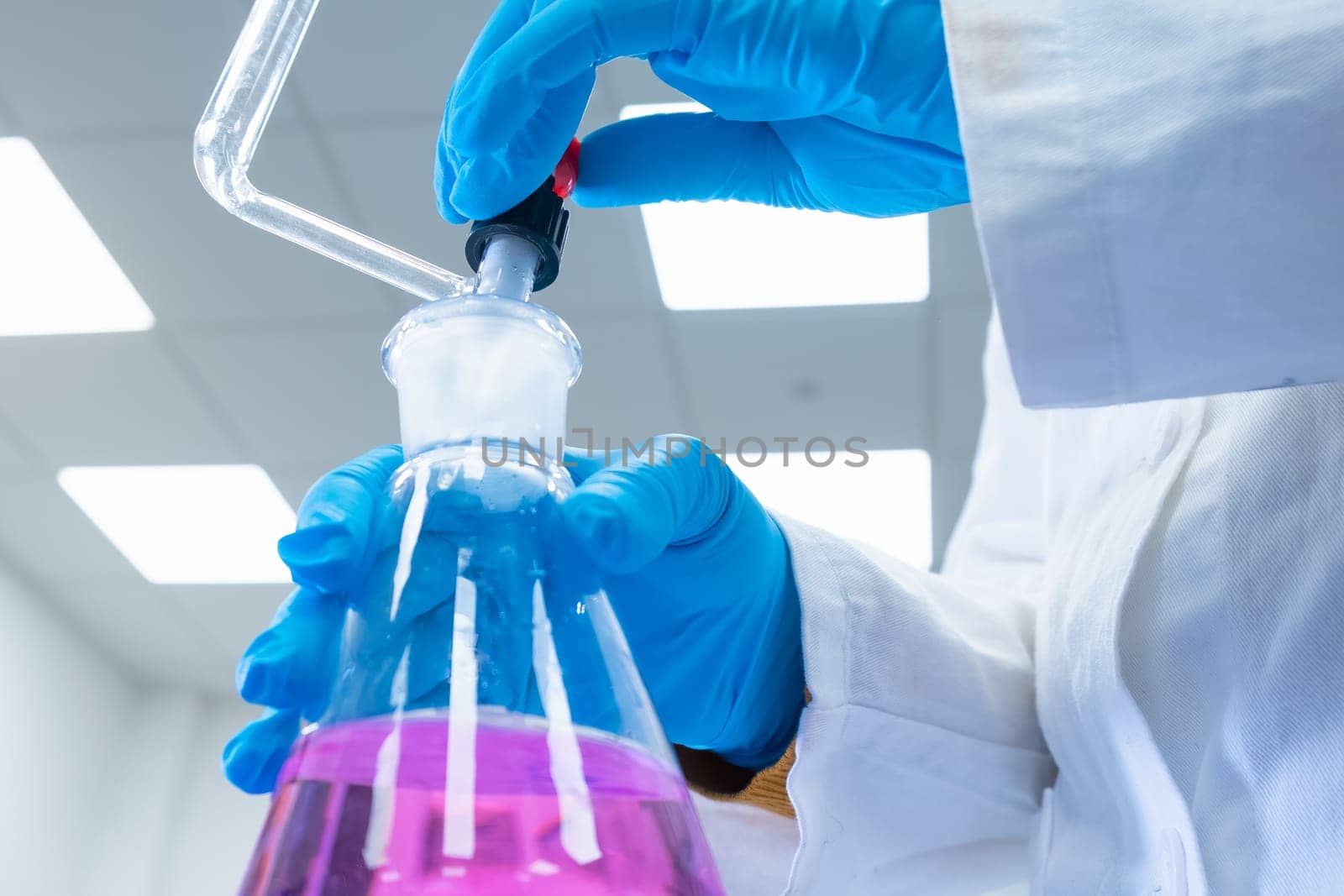 Close up scientist uses a titration method of analysis to study the chemical properties of the water sample. Scientist holding Erlenmeyer flask with pink solution