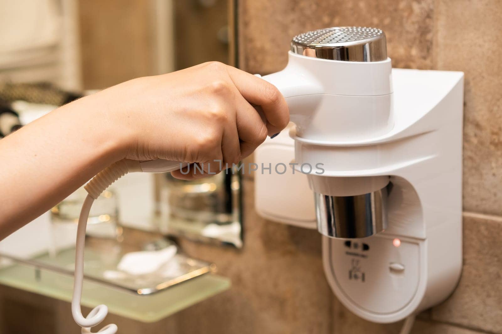 Woman takes a hair dryer with her hand in the bathroom.