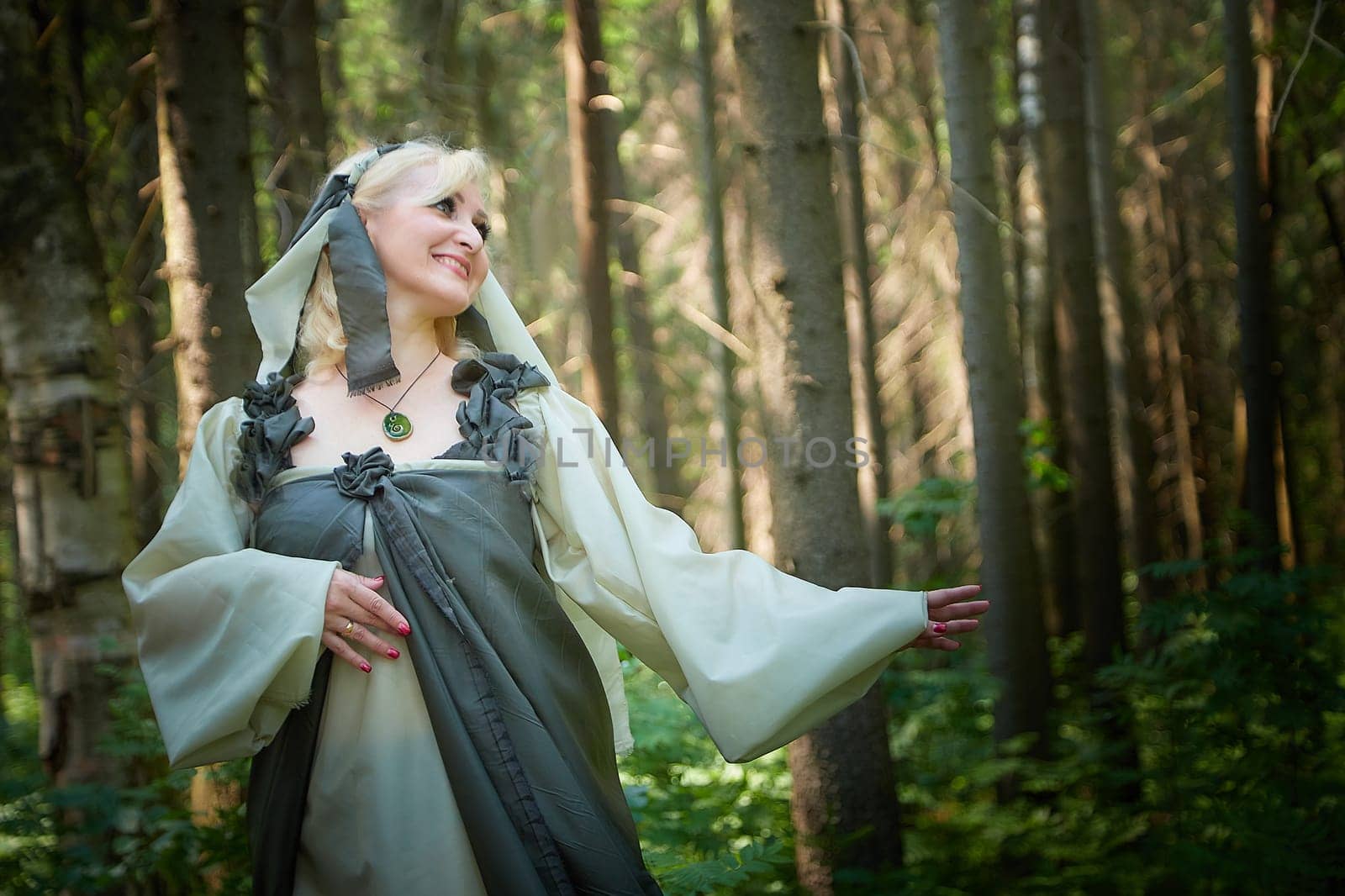 Adult mature woman 40-60 in a green long fairy dress in forest. Photo shoot in style of dryad and queen of nature. Fairy in beautiful green summer forest. Concept of caring for nature