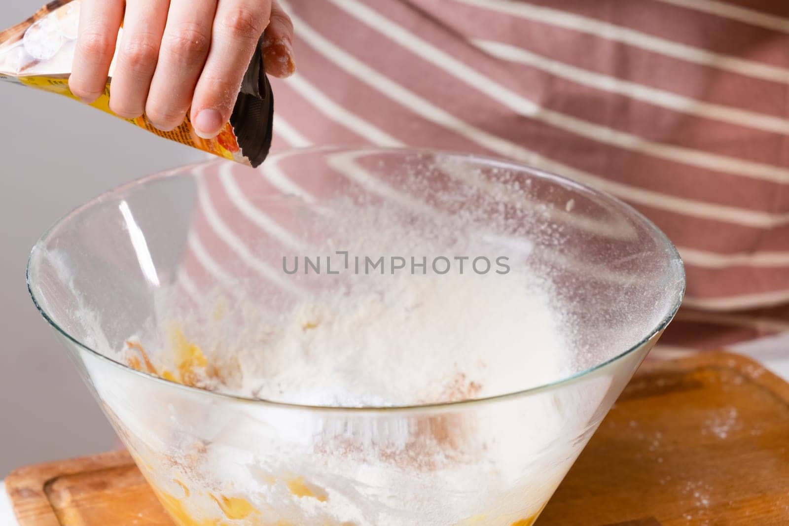 Close up woman sifts wheat flour through a sieve into mixing bowl for dough preparation for cake and bakery on the black background. Knead the dough for homemade pastry.