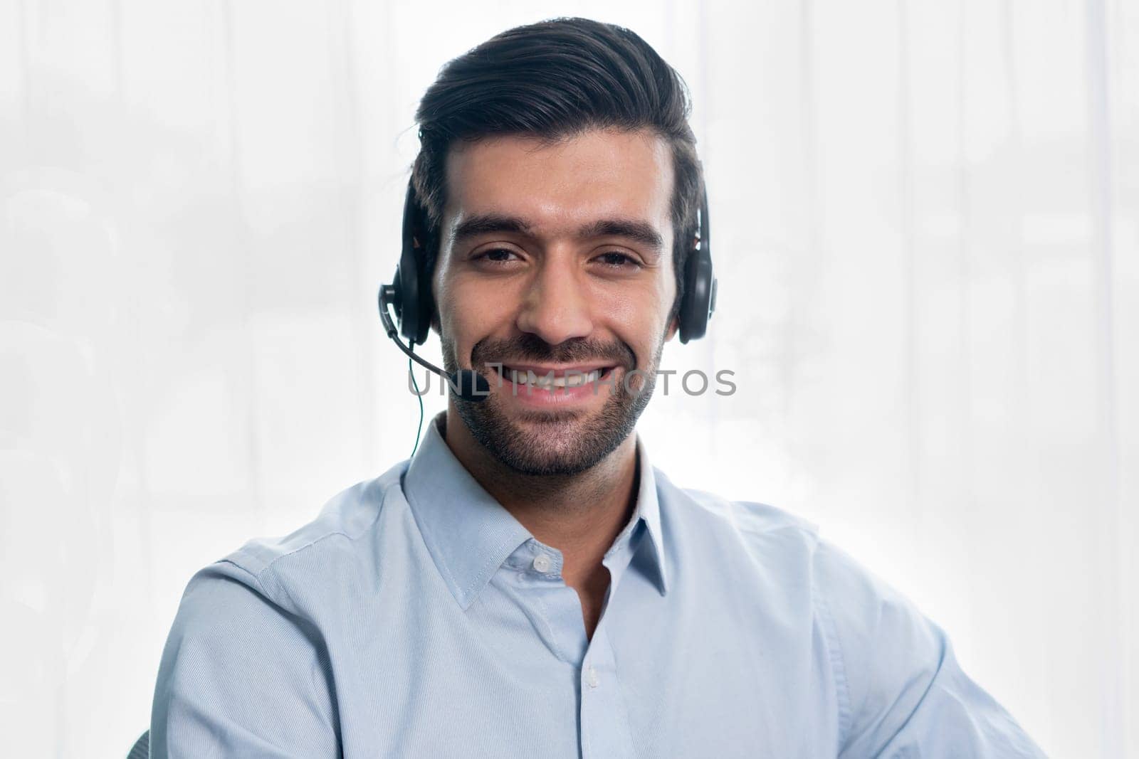 Male call center operator or telesales representative siting at his office desk wearing headset portrait. Customer service agent with smiling to camera on workplace. fervent