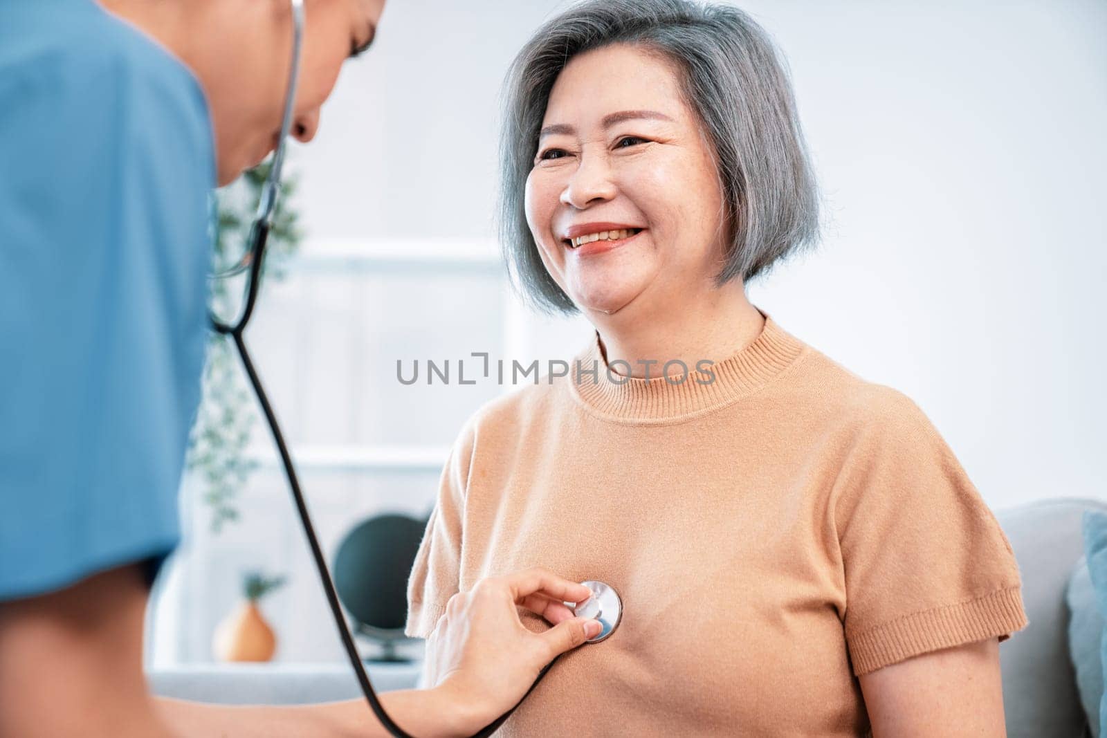 A contented retired senior woman being exterminated by her caregiver with a stethoscope at home. Medical care service, senior care at home.