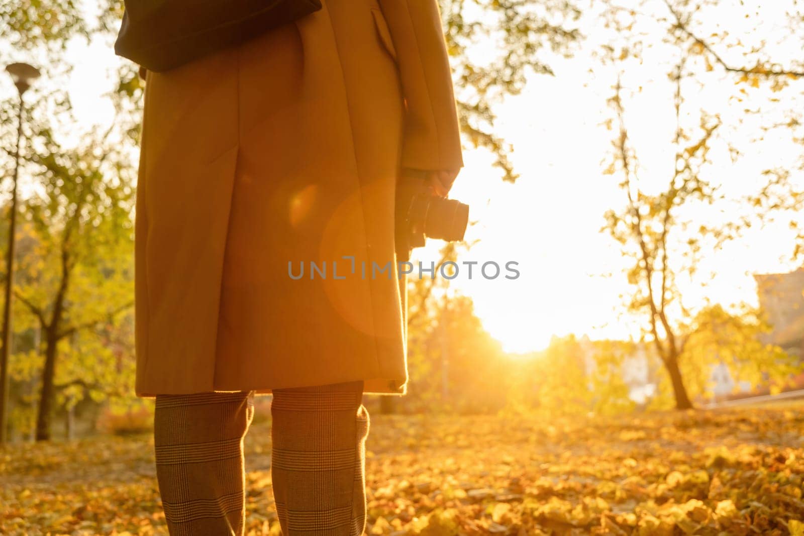 Back view of the woman holding a camera against sunlight in the autumn park