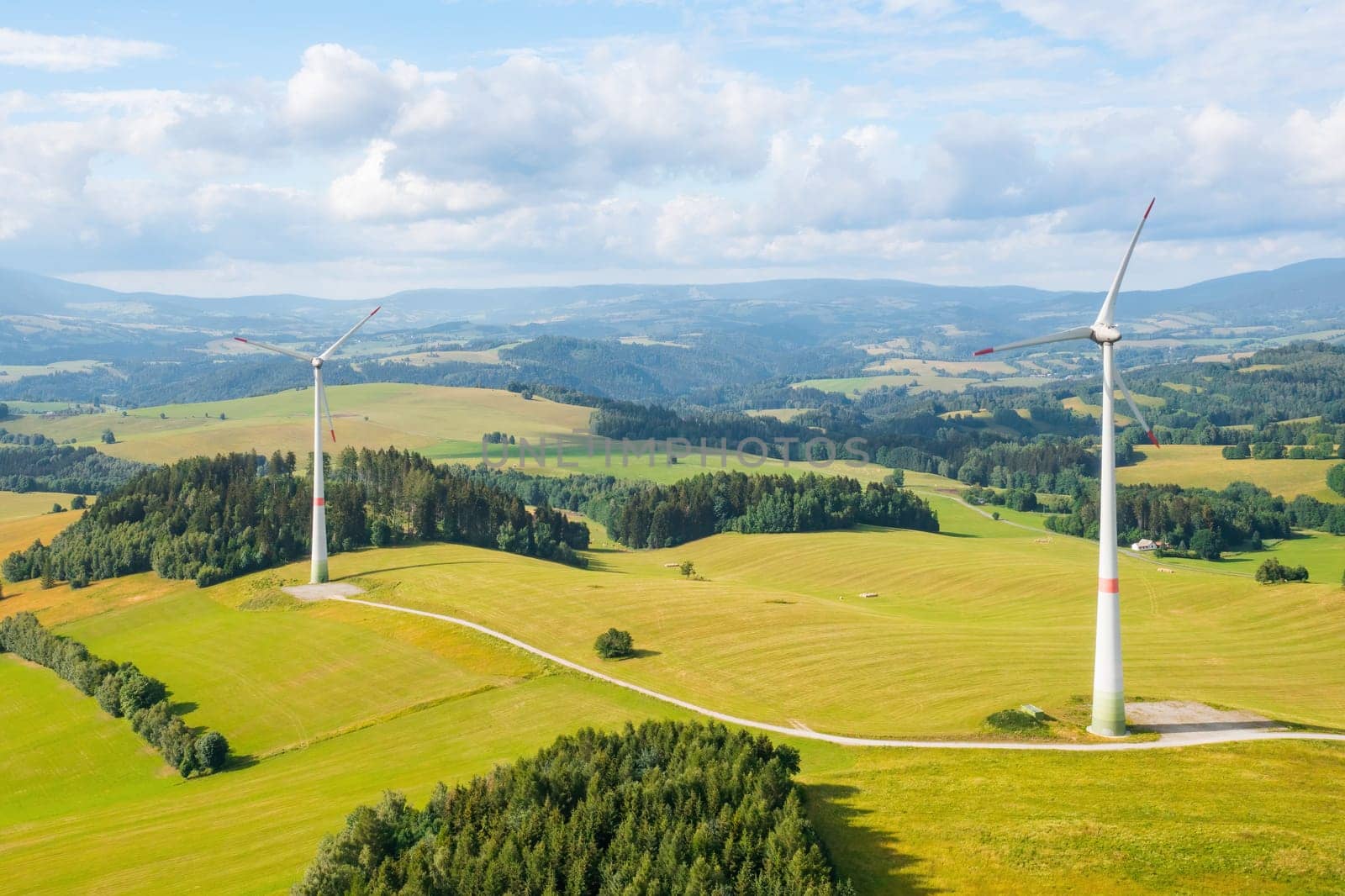 Panoramic view of windmills in the wind farm in the yellow field and mountains on the background. Production of green and renewable energy.