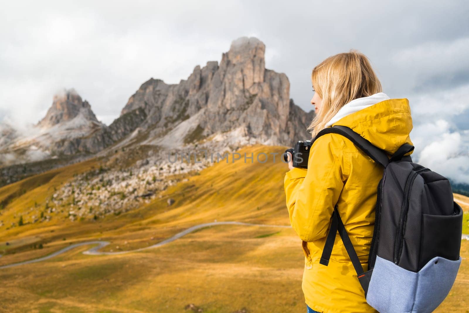 Professional photographer in yellow sport jacket takes pictures of Passo Giau pass using camera. Woman with backpack enjoys activity in Italian Alps