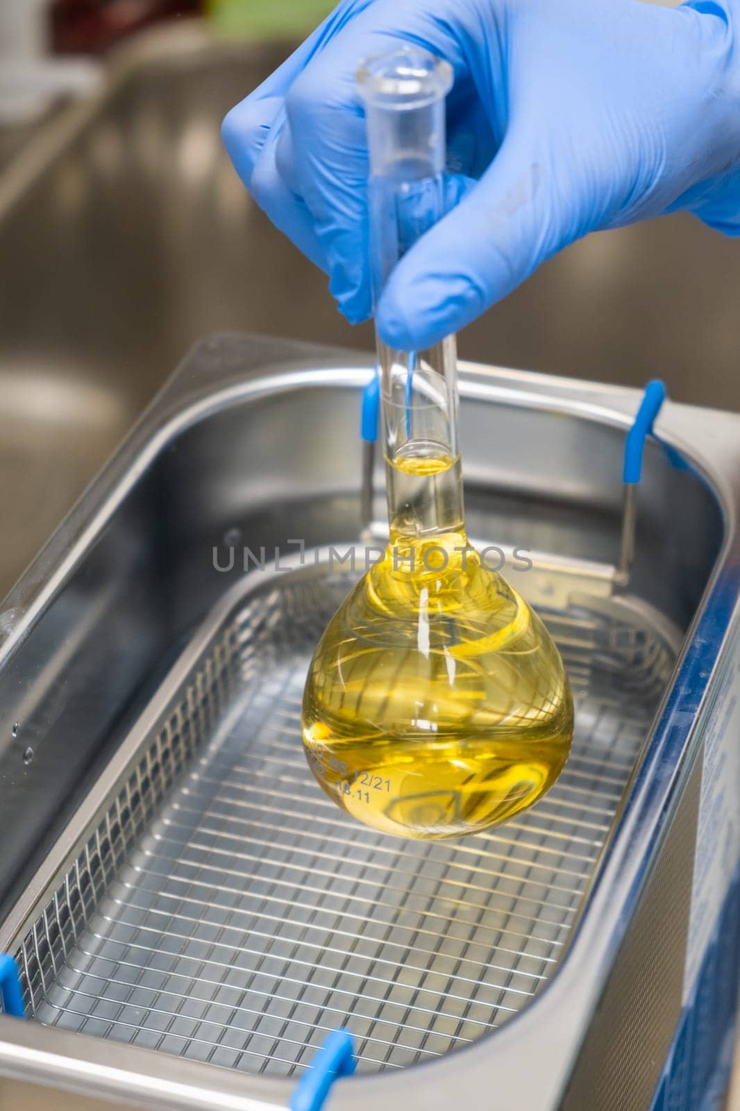 Scientist in blue rubber puts a yellow solution in the flask for dissolving or extraction into ultrasound bath. Urea analysis. Clinical, toxicological and forensic analysis.