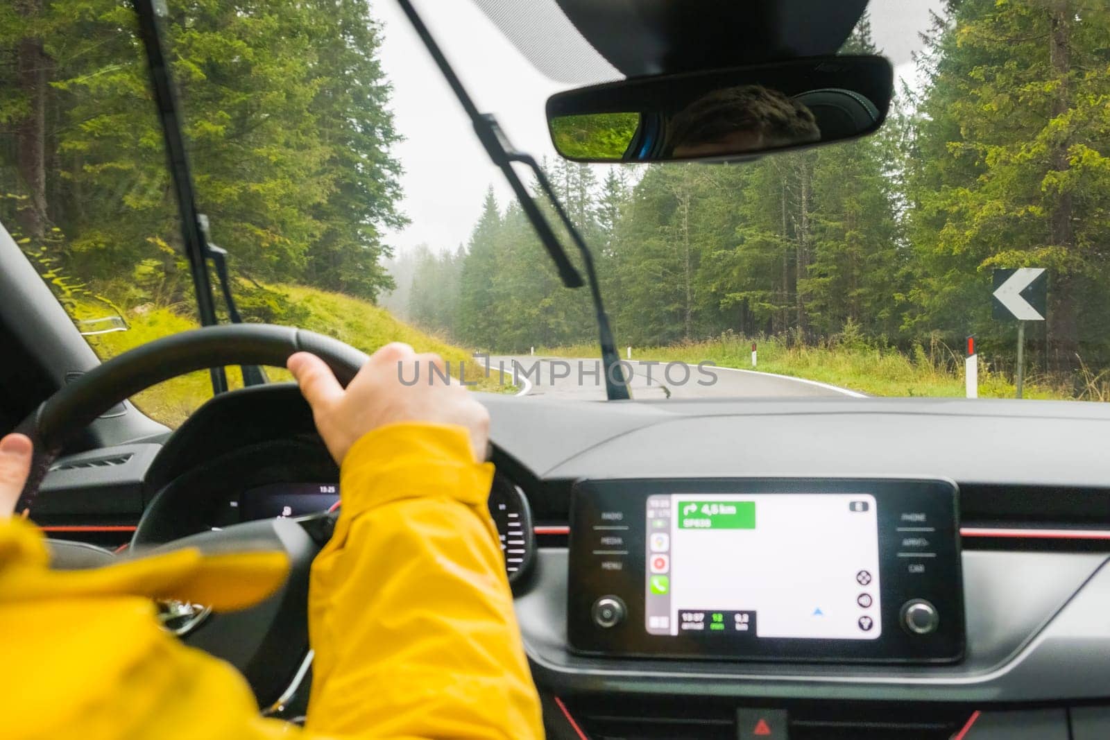 Tourist drives car through pass in Alpine mountains on rainy day. Traveler drives automobile and uses Google maps on winding road among thick trees in mountain forest, January 2023, Belluno, Italy