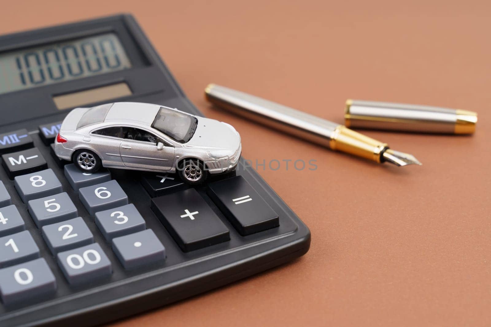 Toy car, calculator and pen on a brown background. Car rental, purchase or insurance. Business concept