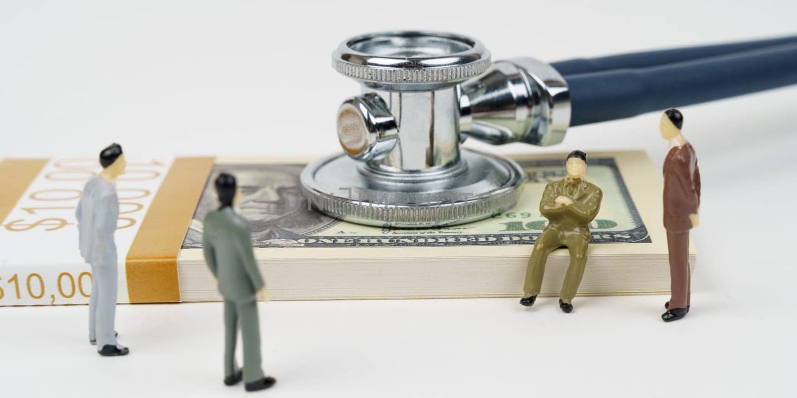 The concept of stagnation in the economy. On a white surface lies a pack of dollars, with a stethoscope on the dollars. Nearby are miniature figures of businessmen.