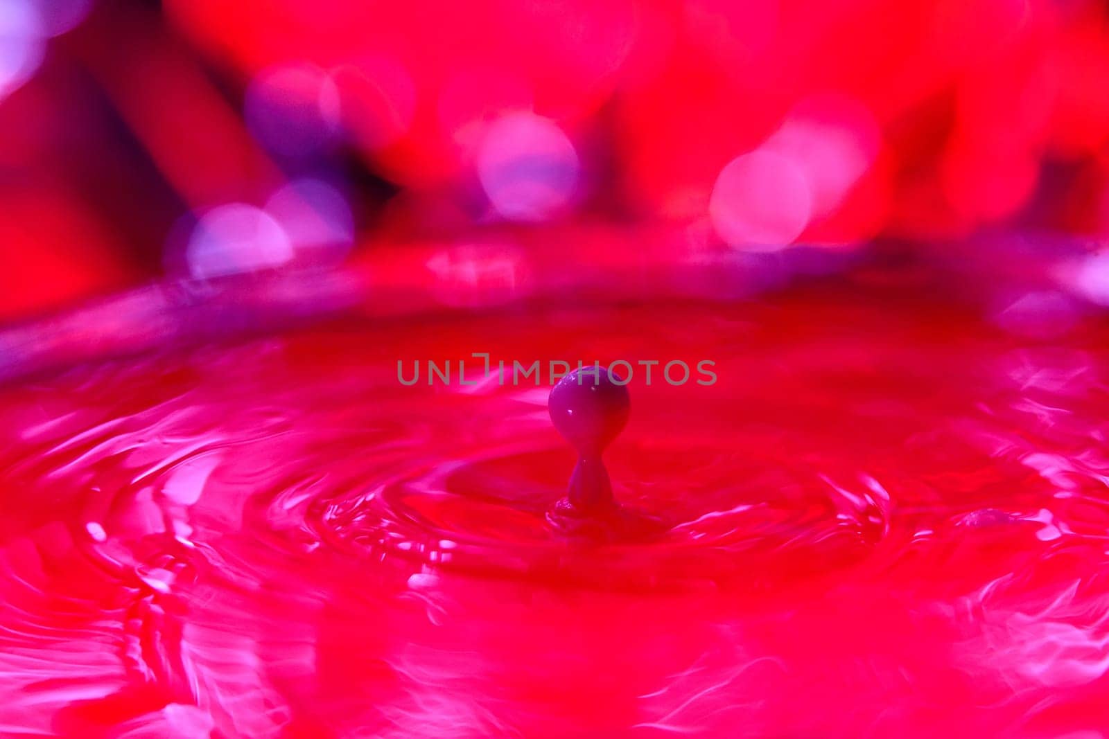 A drop falls into a dense liquid with a red background. Abstract colorful background