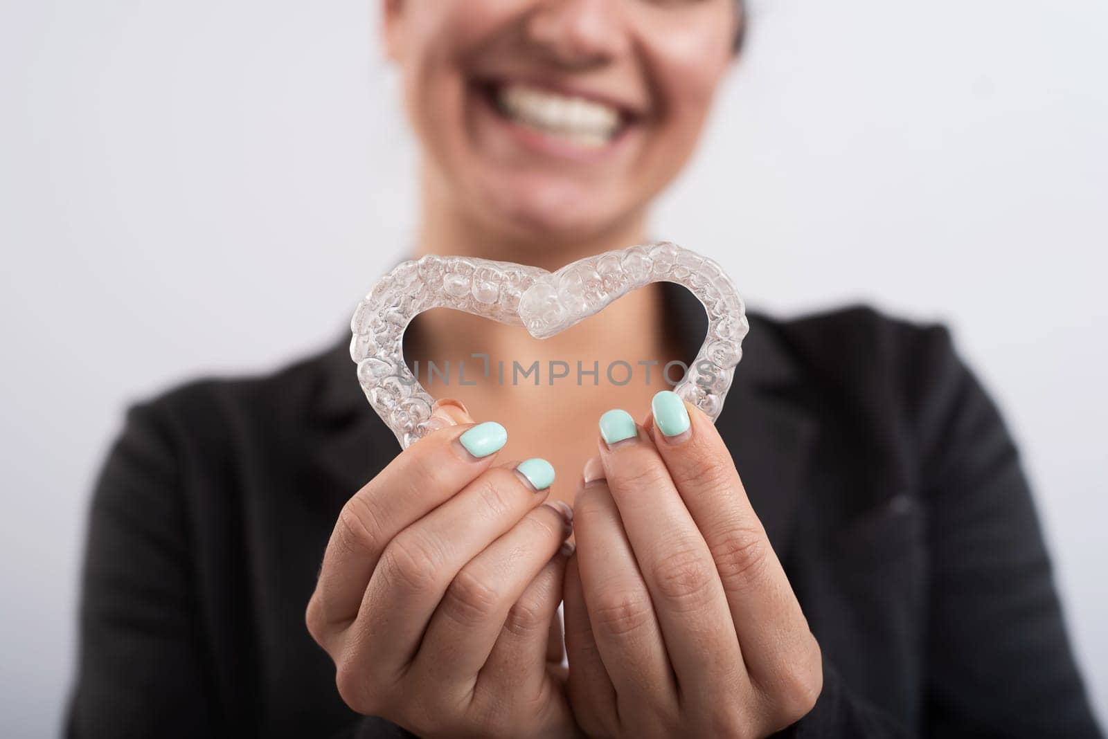 Caucasian woman holding two transparent heart-shaped aligners.