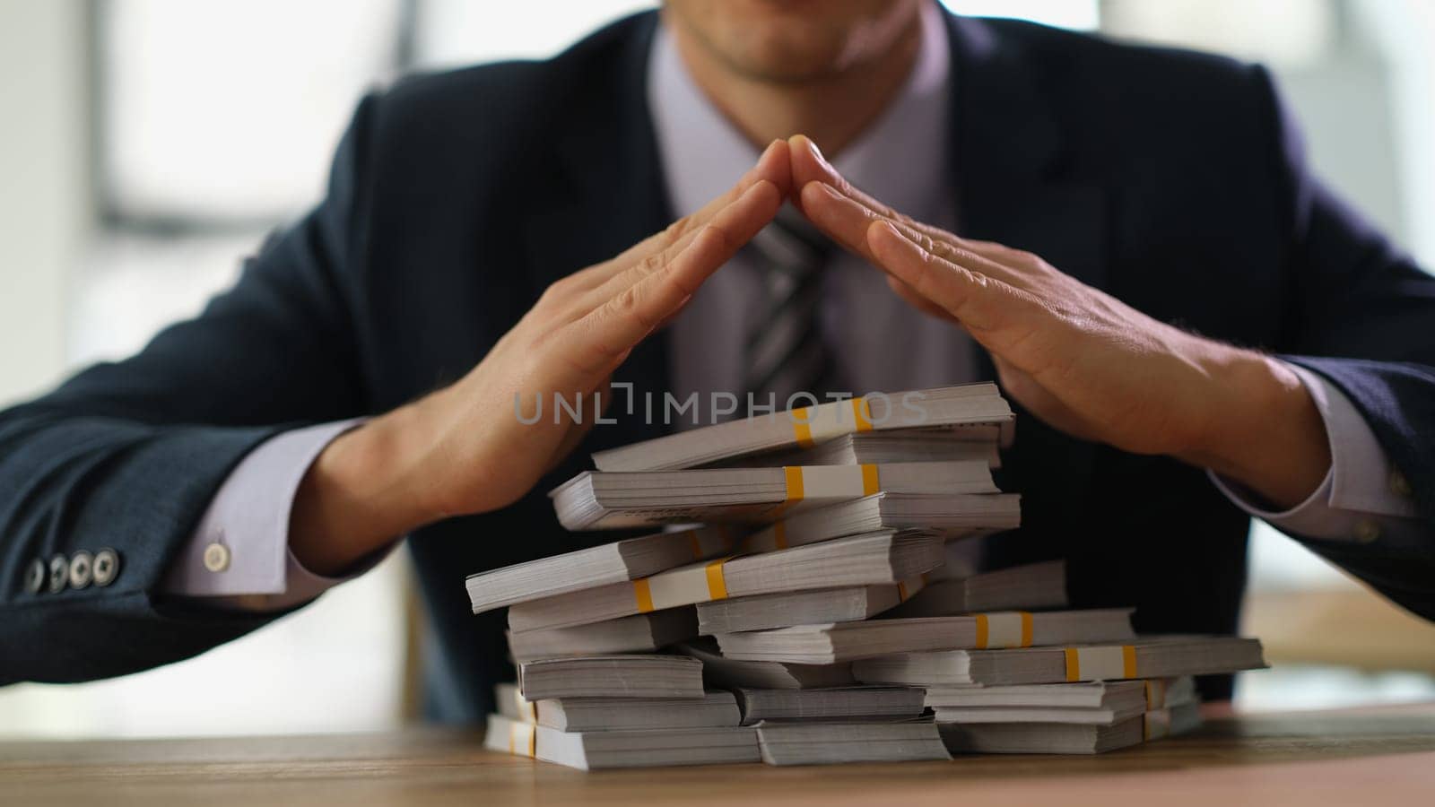 Banker making roof with hands over bundles of dollar bills closeup. Safe storage of money and profitable financial investments concept