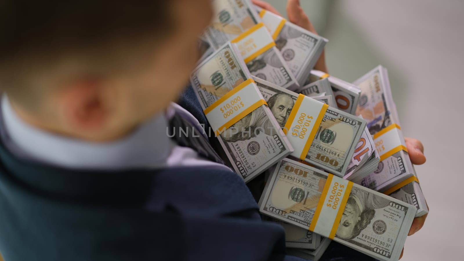 Businessman carrying many bundles of dollar bills closeup. Money transactions and profit growth in business concept