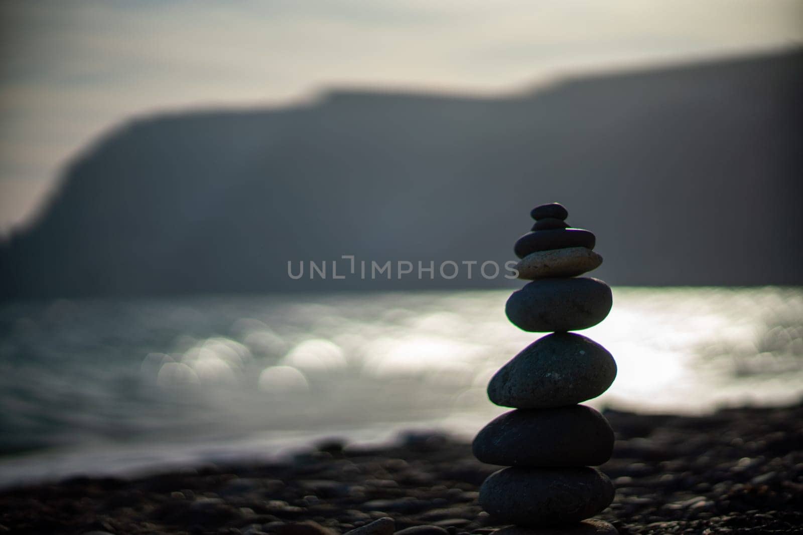 Pebble pyramid silhouette on the beach. Sunset with sea in the background. Zen stones on the sea beach concept, tranquility, balance. Selective focus by Matiunina