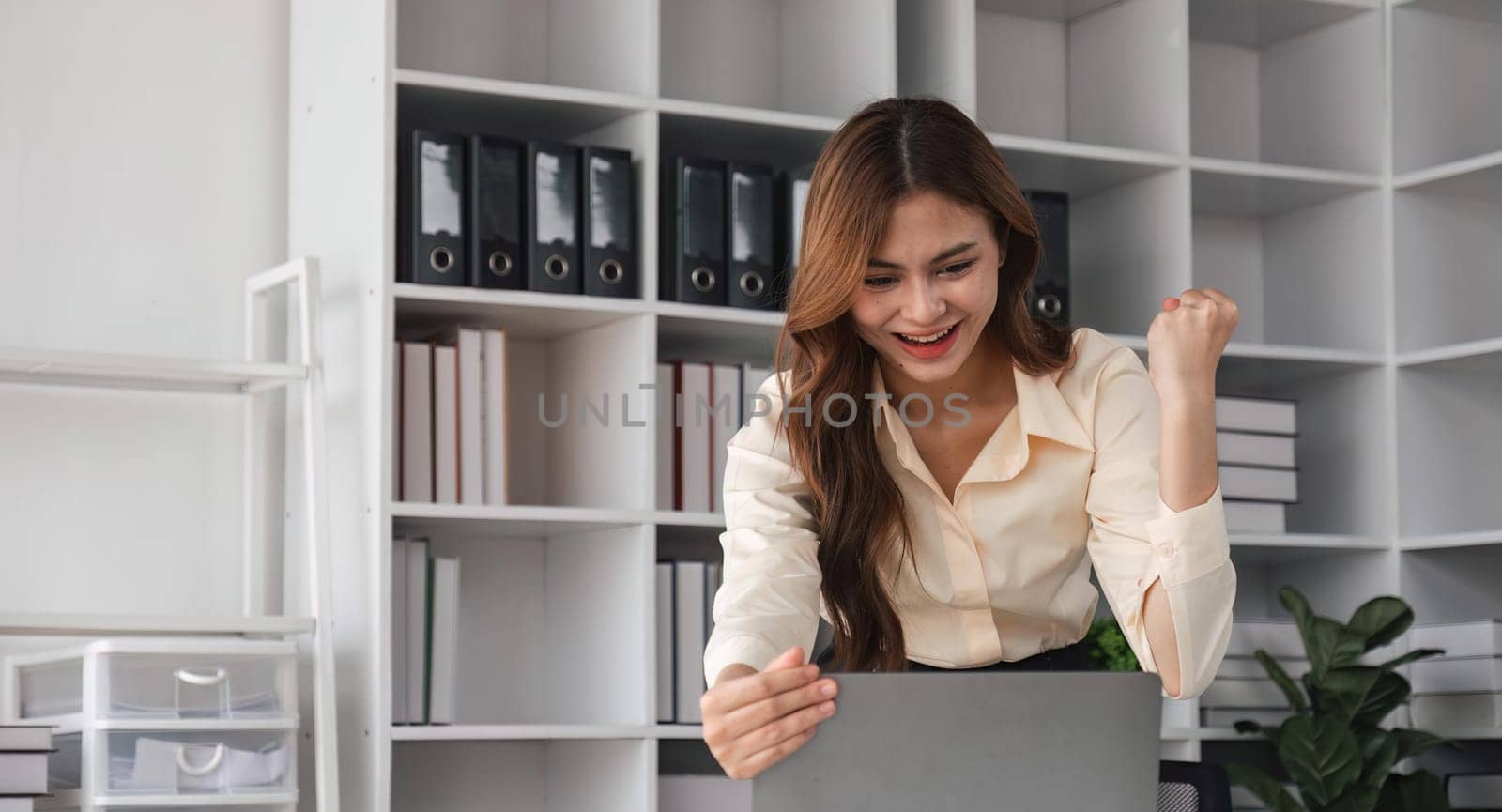 Success at work, good deal. Asian business woman looks at the laptop screen, screams excitedly and raises his fists in a victory gesture by nateemee