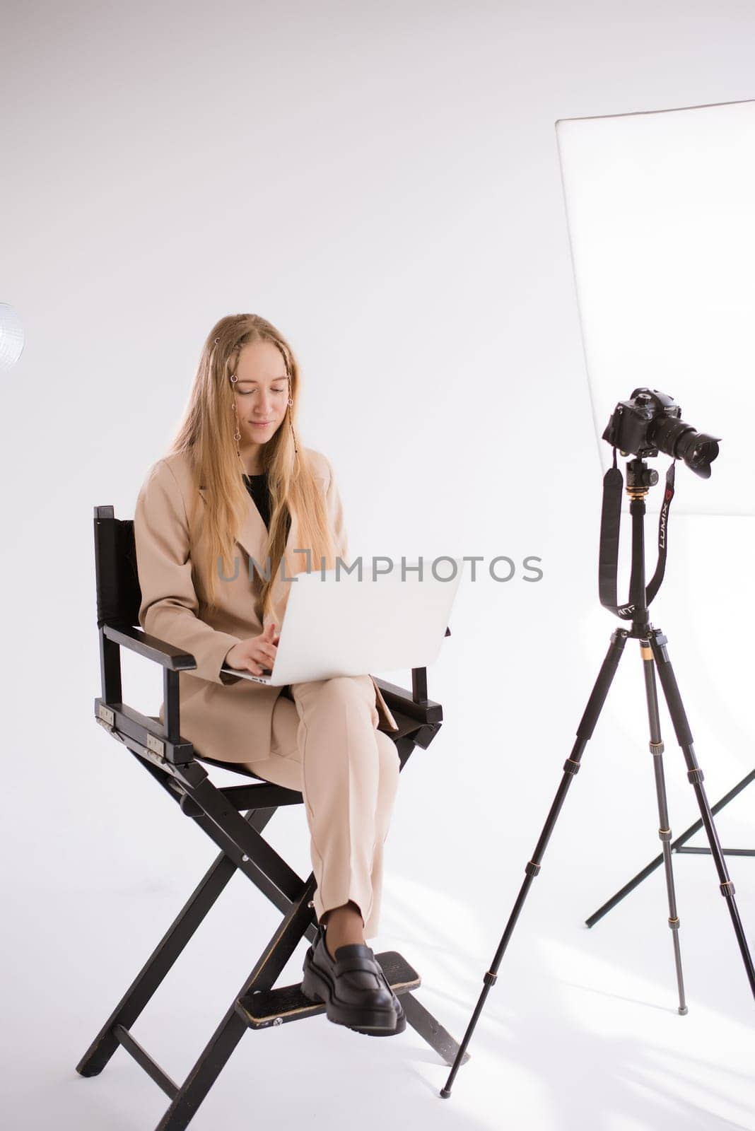 A business woman videographer producer assistant in a suit is working, typing on a laptop and sitting on a chair. Video Production studio, tripod camera