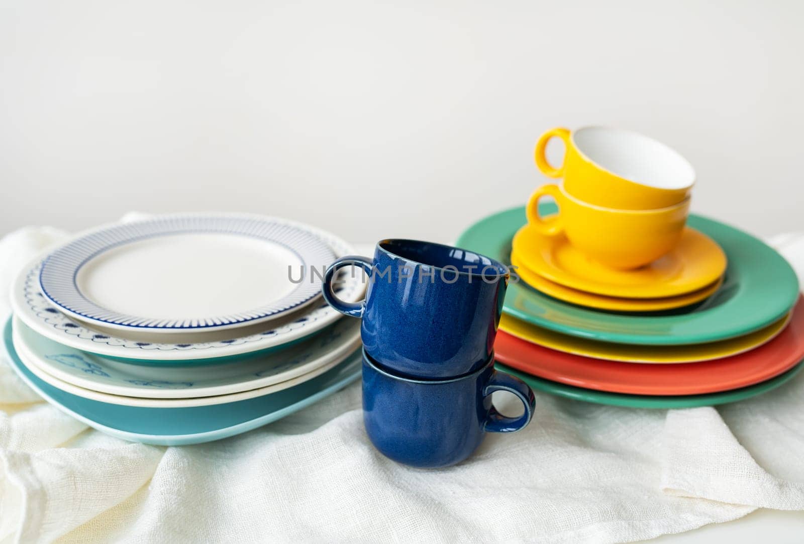 A pyramid of brightly colored bowls, plates and cups of different sizes and colors on the kitchen table. Scandinavian style, minimalism. Preparation for dinner with loved ones