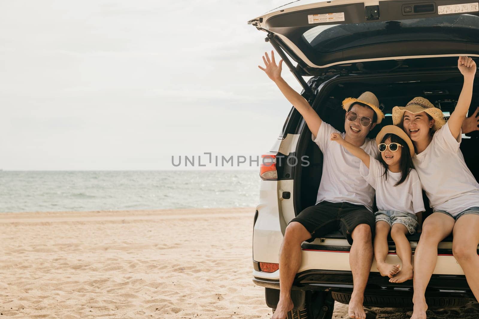 Happy Family Day. Dad, mom and daughter enjoying road trip sit on back car and raise hand up, Family traveling in holiday at sea beach, people having fun in summer vacation on beach with automobile