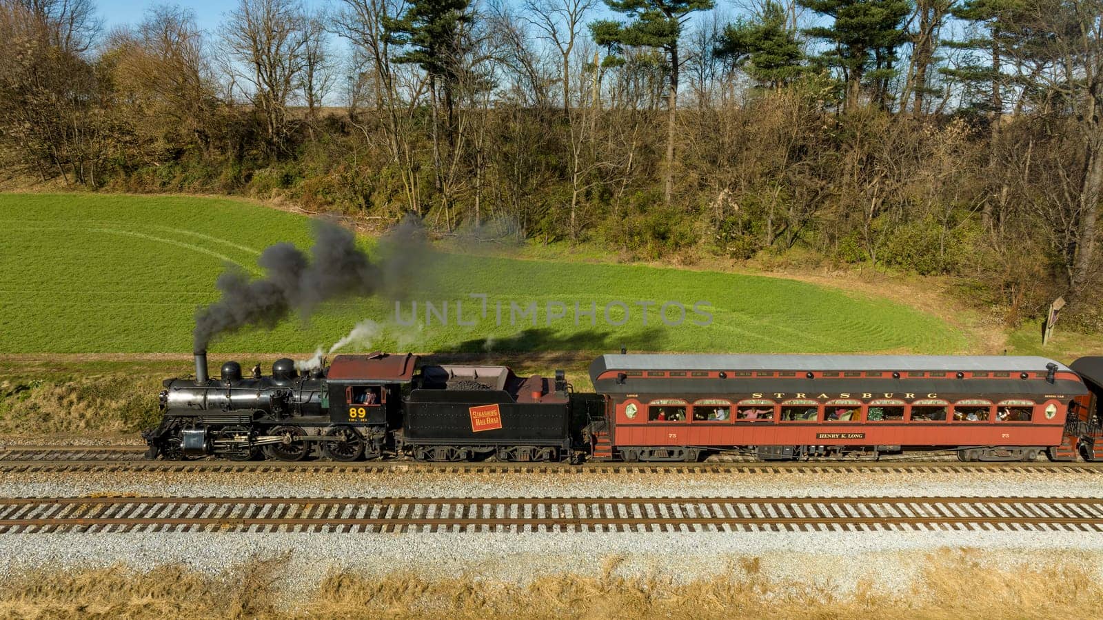 Ronks, Pennsylvania, November 26, 2022 - A Drone View of a Restored Steam Passenger Train Traveling Thru Farmlands Pulling Up to a Small Station on an Autumn Day